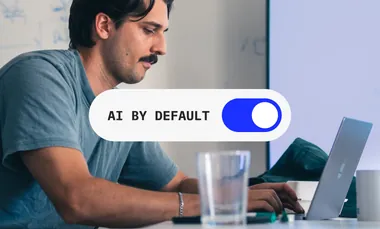 Enablement, das ohne Antrieb weiterläuft: Arbeit am Laptop, darüber der Schalter „AI by Default“ in Stellung an.