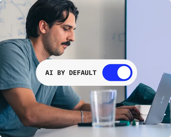 Enablement, das ohne Antrieb weiterläuft: Arbeit am Laptop, darüber der Schalter „AI by Default“ in Stellung an.