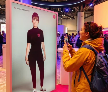 Besucherin des Mobile World Congress fotografiert MIA auf dem Bildschirm mit dem Smartphone