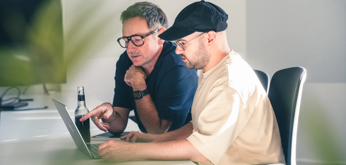 Zwei Männer arbeiten gemeinsam an einem Laptop.